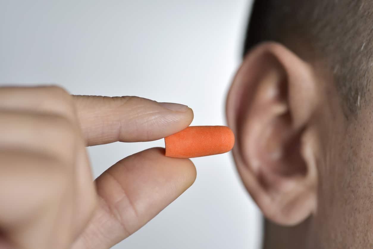 A man inserting an earplug into his ear to protect his hearing.