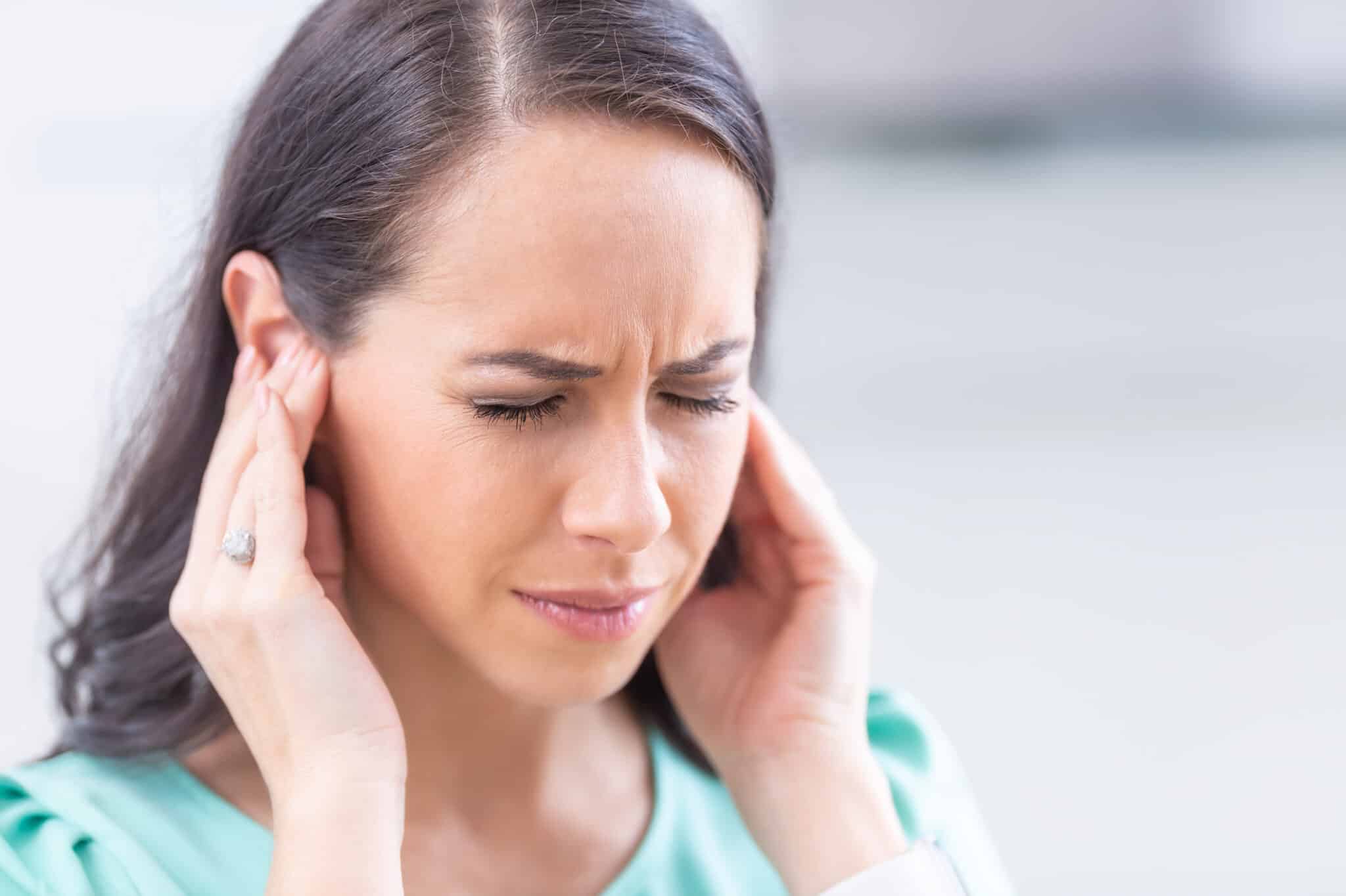 Young woman puts fingers over ears with a painful look on her face