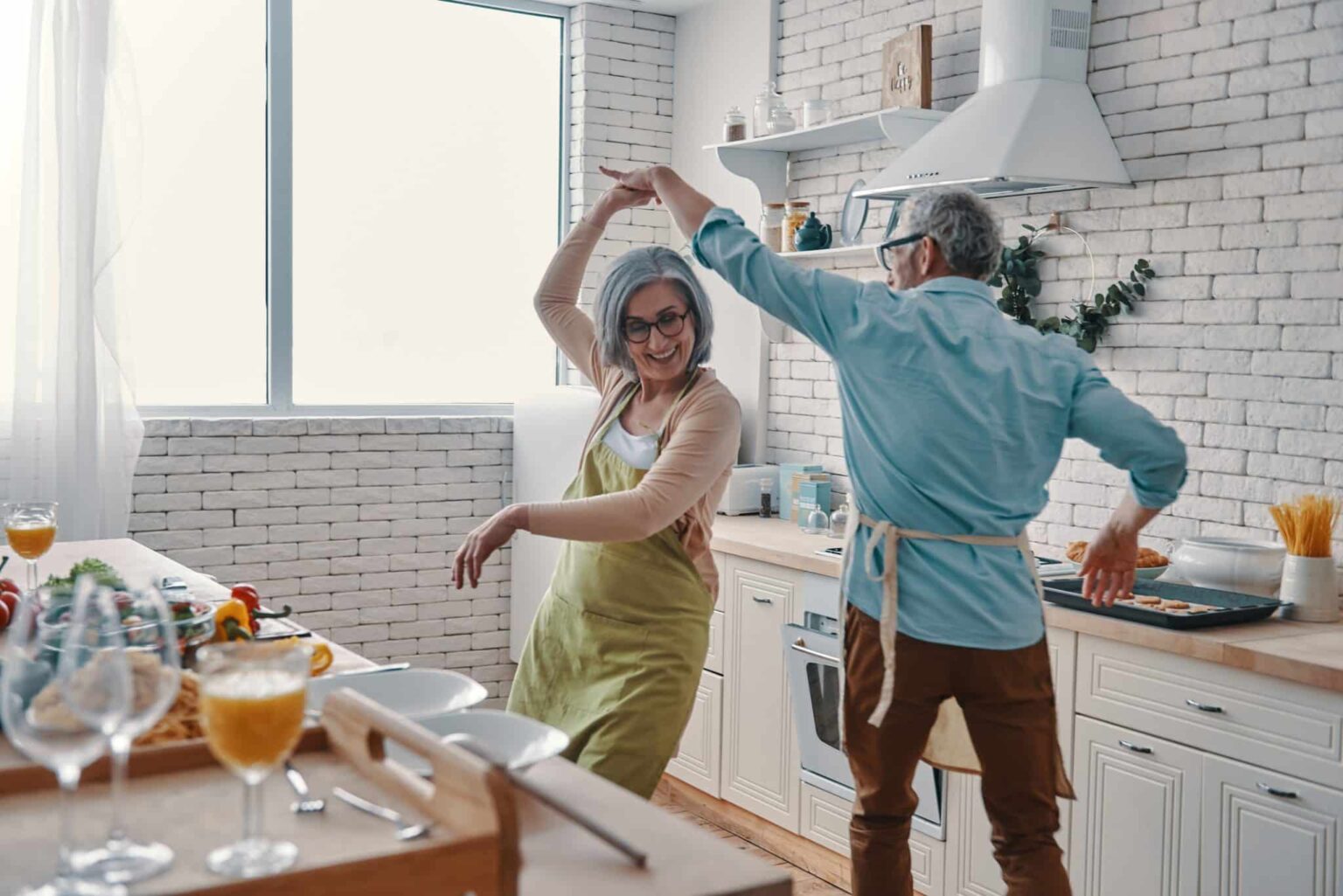couple treating hearing loss with implants Older woman and her husband dancing in the kitchen while preparing dinner.
