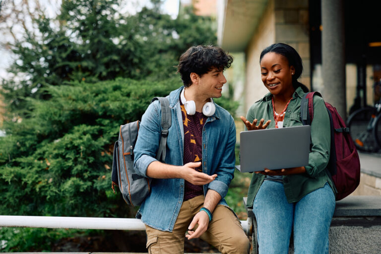 Happy university students e-learning while using laptop at campus. College students reviewing their notes on a laptop