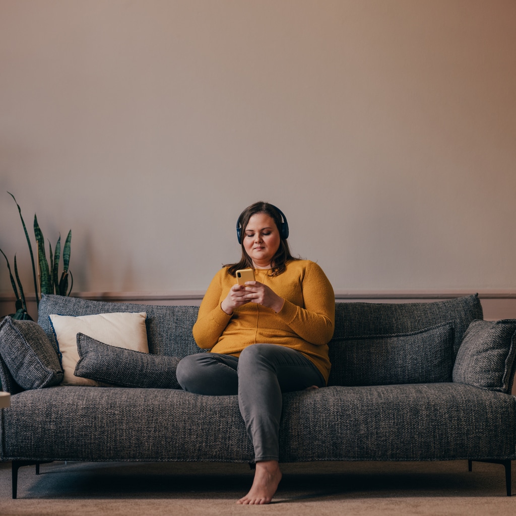 Woman sitting on a couch listening to an audiobook through headphones