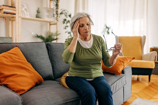 Older woman with Ménière's disease experiencing a dizzy spell, sitting down on the couch until it passes.