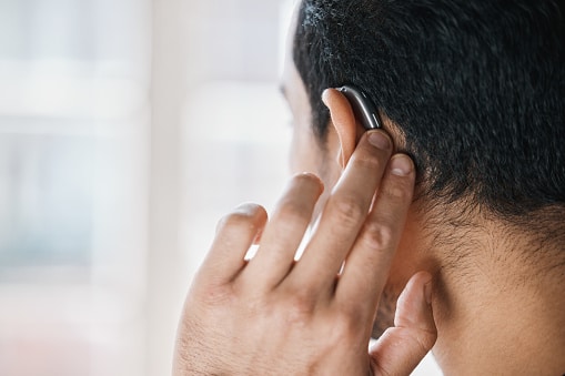 Man with hearing aids touches his hearing aid, trying to fix feedback issues.