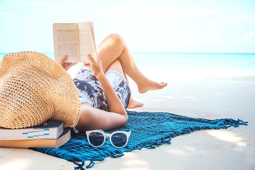 Woman reading a book on a beach on a summer's day.