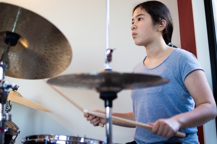 A candid photograph of a girl playing on a drum kit